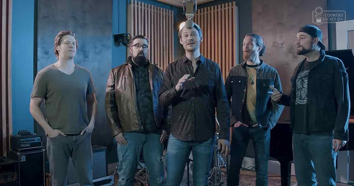 A recording studio scene with five adult males, variously dressed in casual attire, engaged in a session with soundproofing panels on walls and equipment visible.