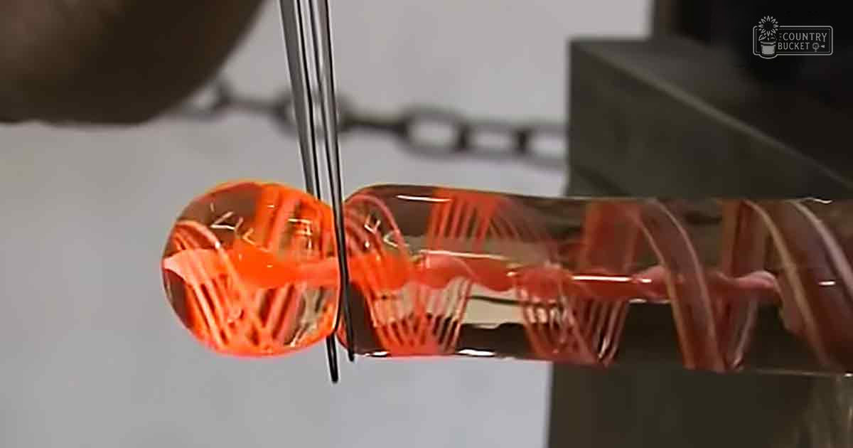 Molten glass being shaped by tongs in a workshop environment