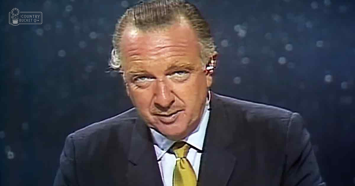A middle-aged male in a formal dark blue suit with light blue shirt and yellow tie, set against a professional studio backdrop with bokeh lighting.