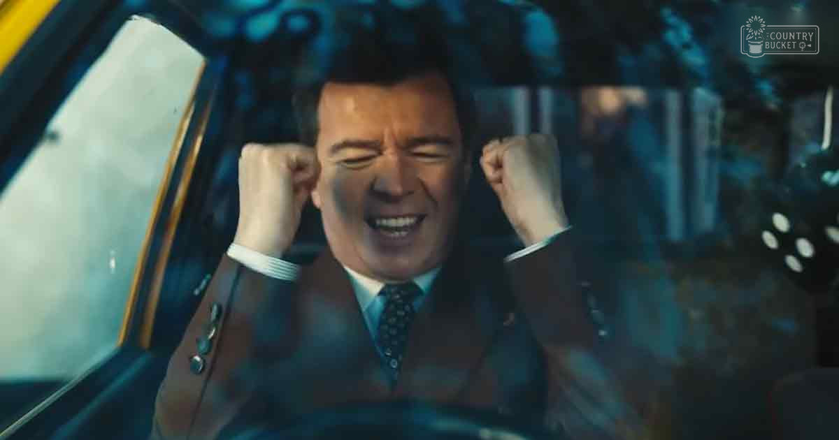 A middle-aged adult male in a dark suit jacket stands against an urban nighttime backdrop.