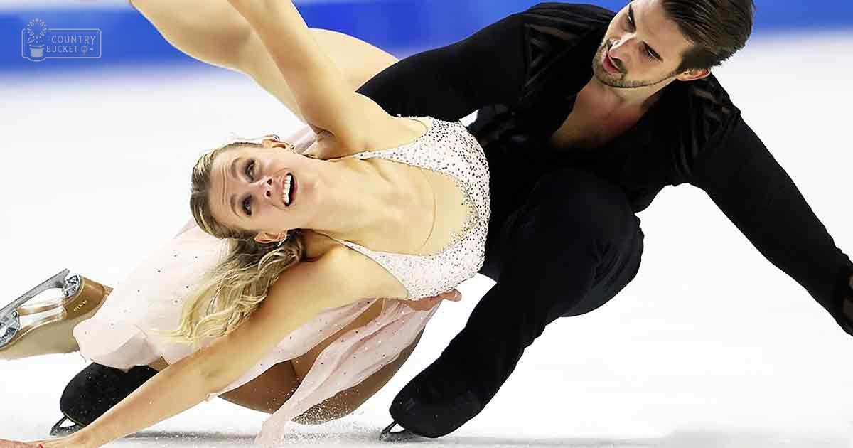 A figure skating pair performing at an indoor ice rink with a blue and white color scheme, well-lit and likely during daytime.