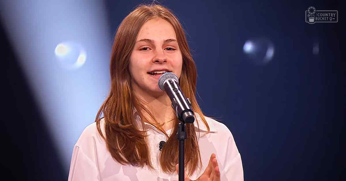 Young adult female wearing a relaxed fit, white button-up shirt with collar and short sleeves, standing indoors near stage equipment under artificial lighting.
