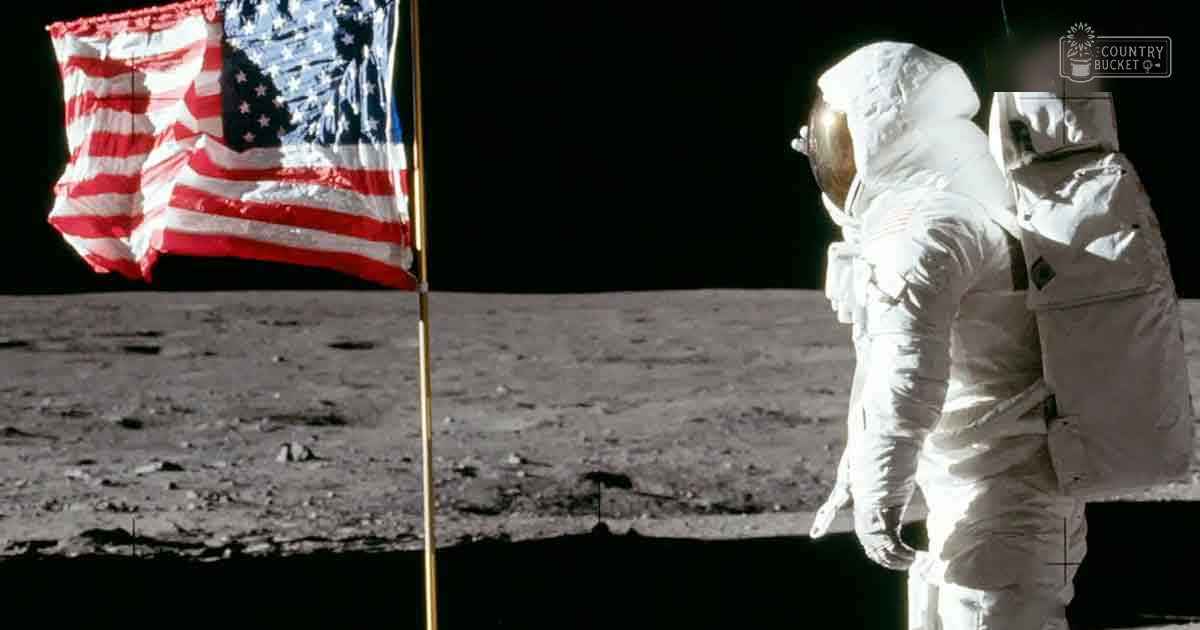 An astronaut in a spacesuit standing beside an American flag on the lunar surface with gray rocky terrain as background