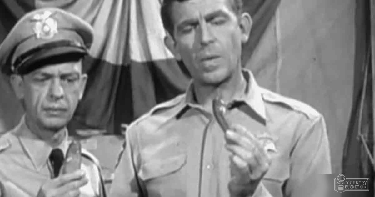 An adult male in a World War II-era U.S. Army uniform stands indoors near another person also wearing military attire; setting appears to be under a tent or幕布 with natural daylight.