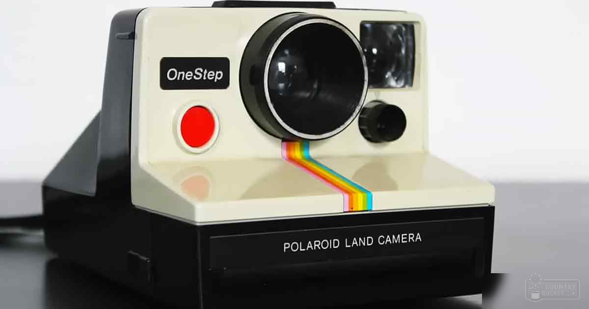 A Polaroid OneStep Land Camera with a rainbow-colored light beam, set against a plain white background indoors.