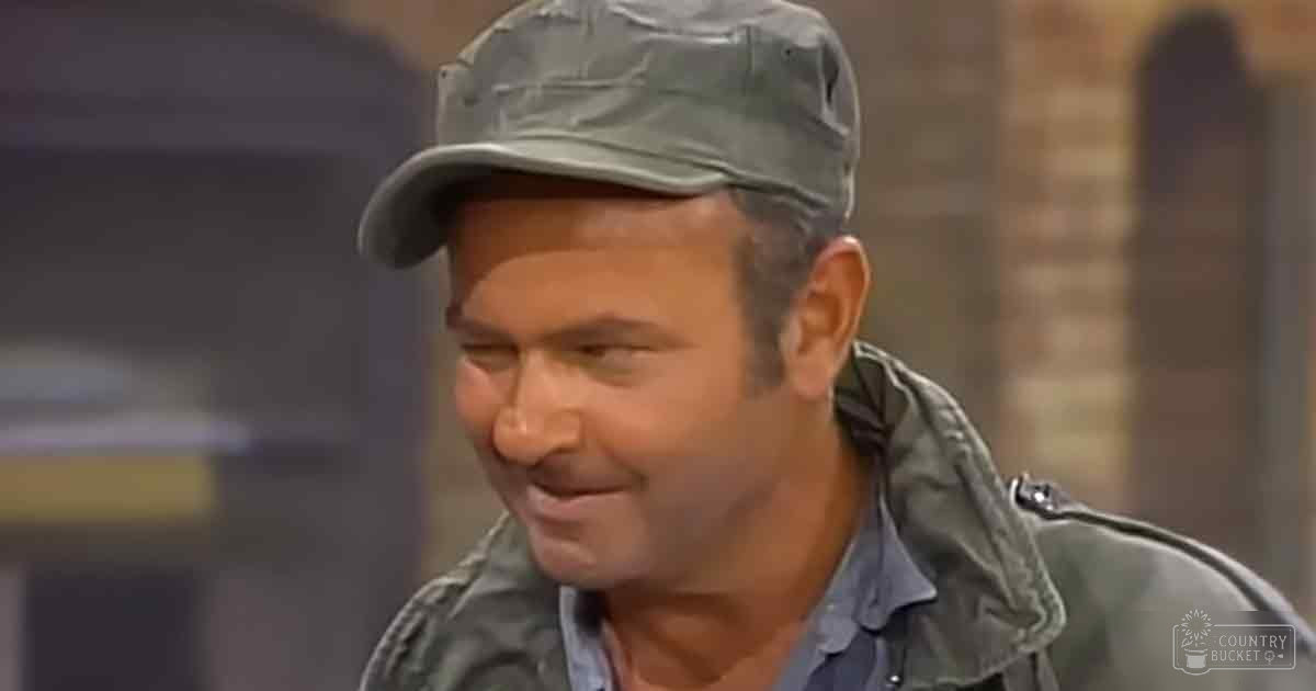A middle-aged adult male wearing a military-style cap and dark green jacket with brick walls in the background, suggesting an indoor setting.
