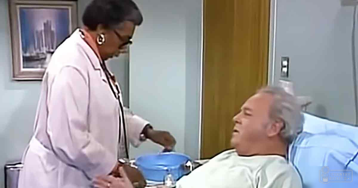 A healthcare professional in a white lab coat attends to an older adult male patient wearing a hospital gown in a clinical hospital room with framed urban artwork and neutral lighting.