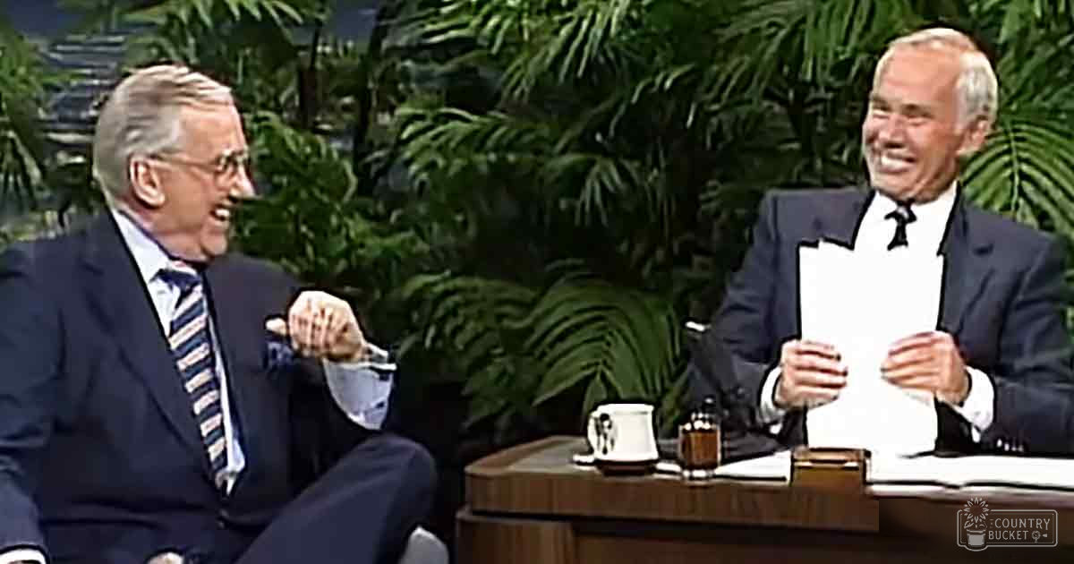 Talk show setting with two older adults in formal attire, lush green background suggesting an outdoor backdrop, indoor studio lighting.