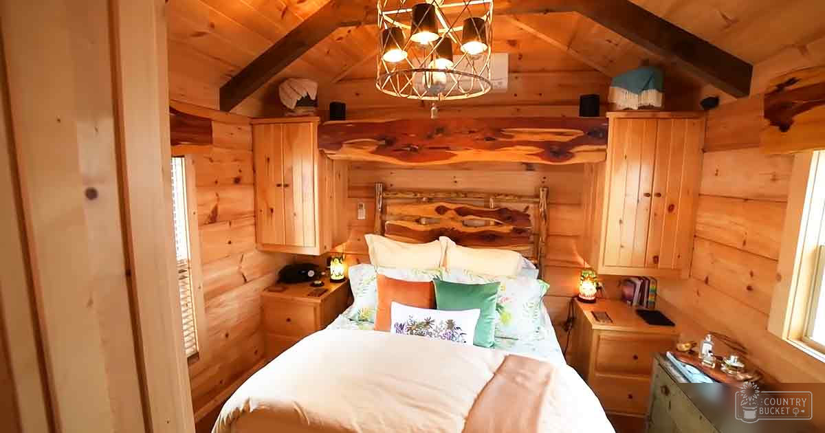A cozy cabin interior with rustic wooden furniture, a bed adorned with colorful bedding, and natural light streaming through windows.