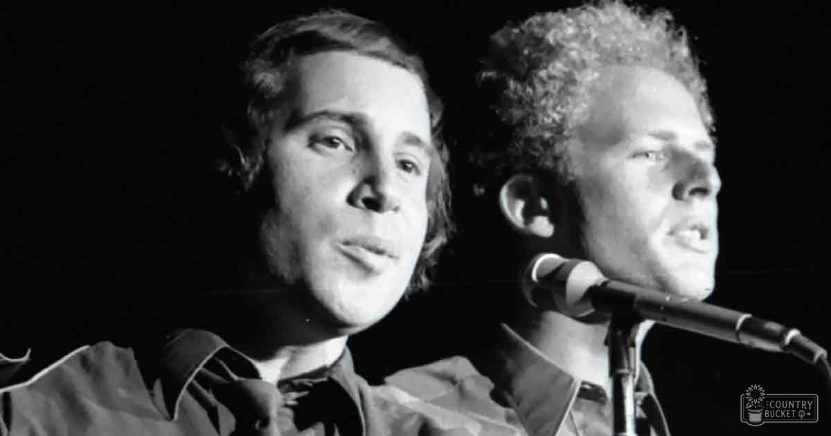 A musical performance scene with young adult males in casual 1970s attire under dim stage lighting, monochromatic black and white photo.