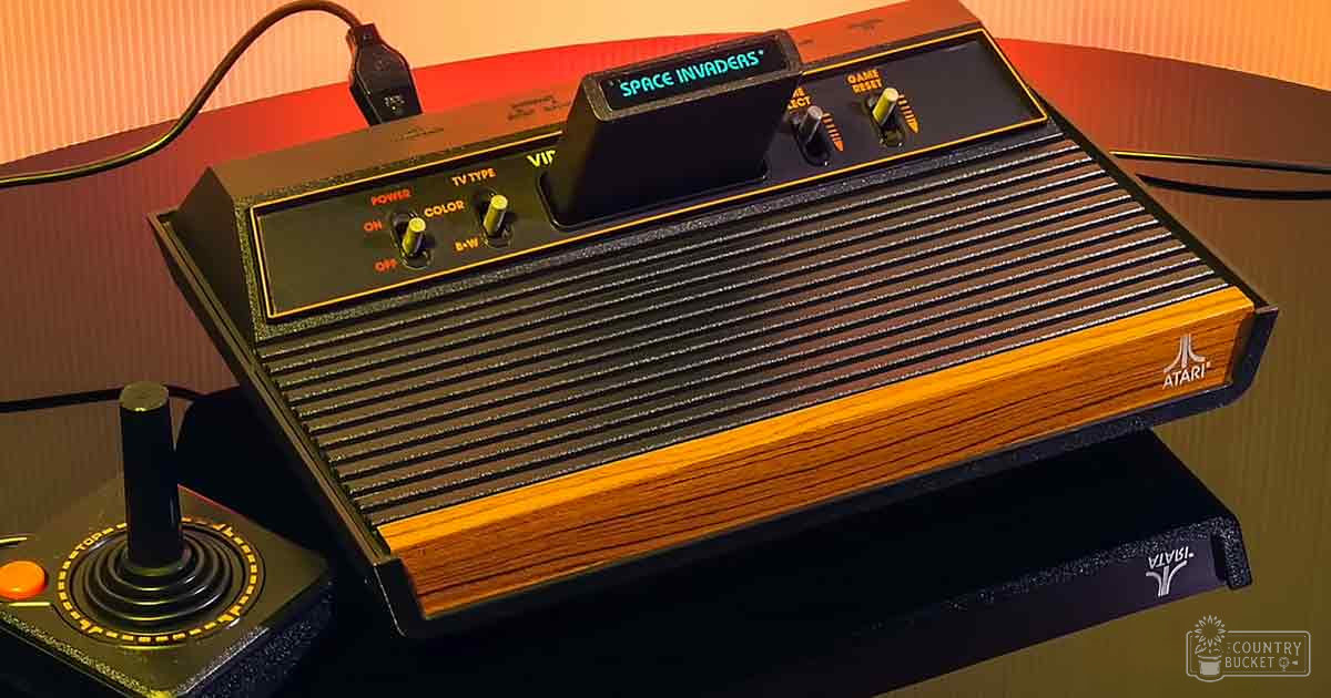 Vintage Atari 2600 video game console with 'Space Invaders' label, wooden panel design, control knobs, and matching joystick controller indoors against a red background.