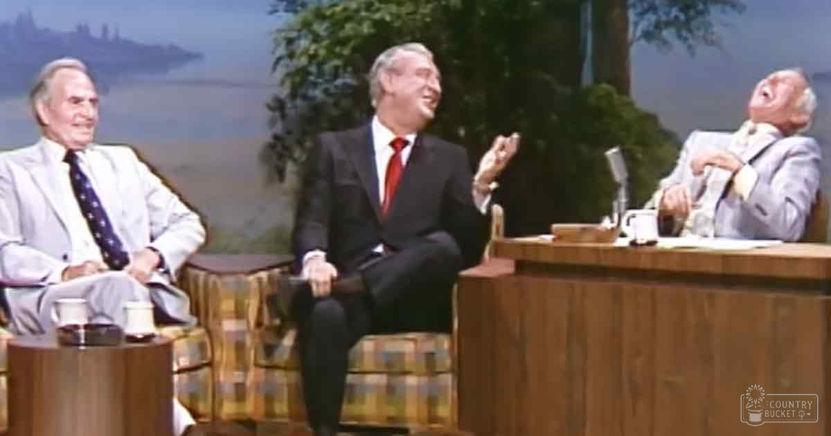 A scenic view with trees and water as backdrop, suggesting an indoor studio setting for a talk show or interview program.