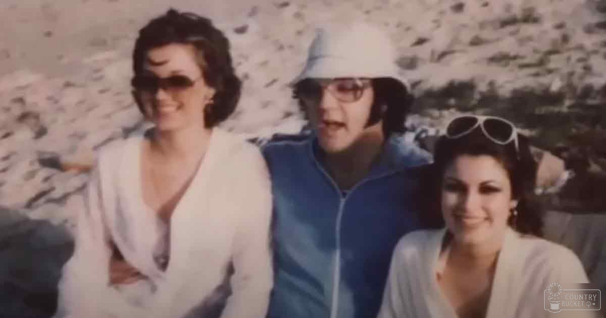 A group of three adults outdoors in casual summer attire, with muted tones and natural lighting.