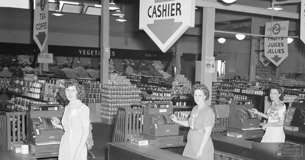 Three women shopping in an old-fashioned grocery store with vintage attire; a cash register and signs for tea/coffee, vegetables, and fruits visible.