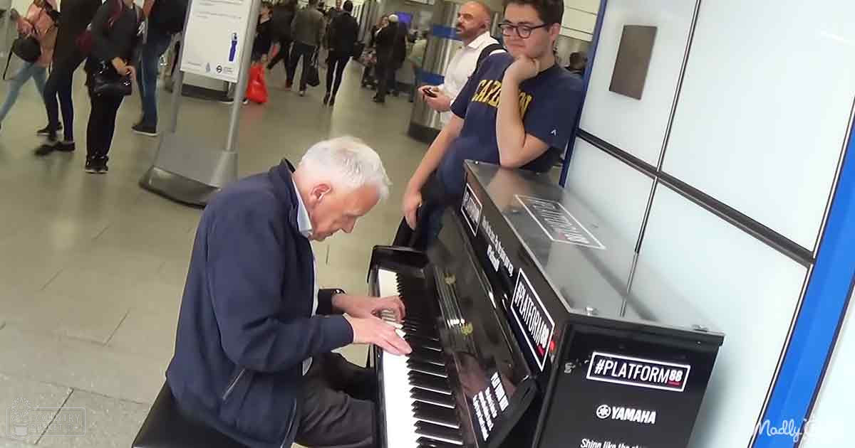An older adult male singer plays a black Yamaha piano labeled 'PLATFORM88' on a subway station platform with other passengers walking by.