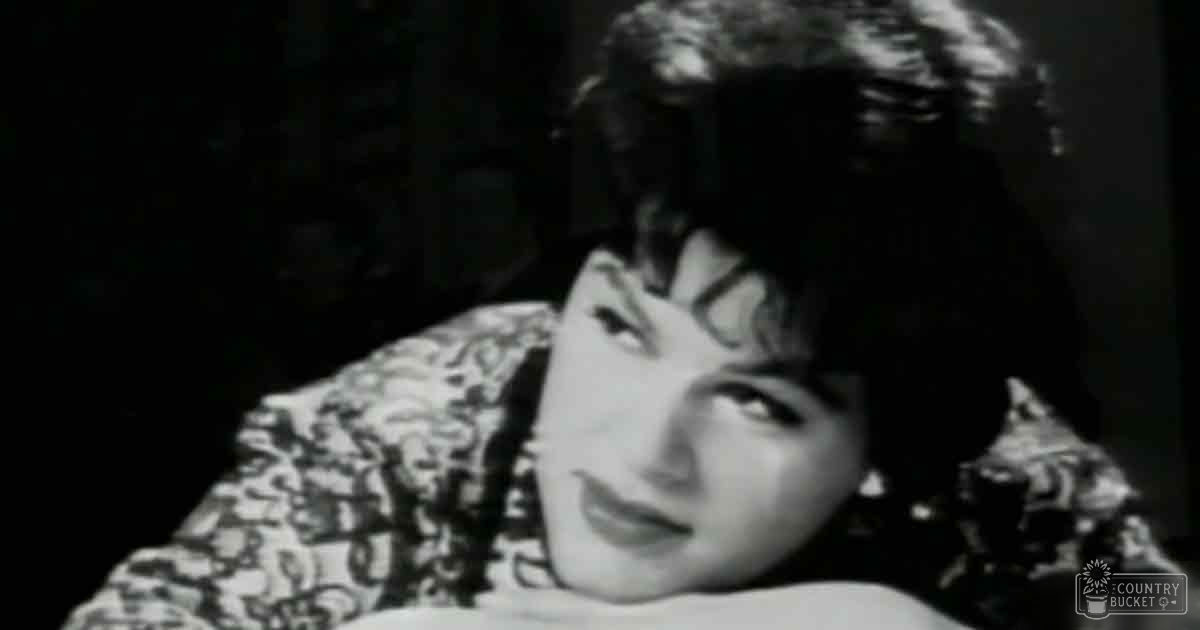 A young adult female in a form-fitting, patterned dress with high neckline and long sleeves, set against a dark background with dramatic lighting.