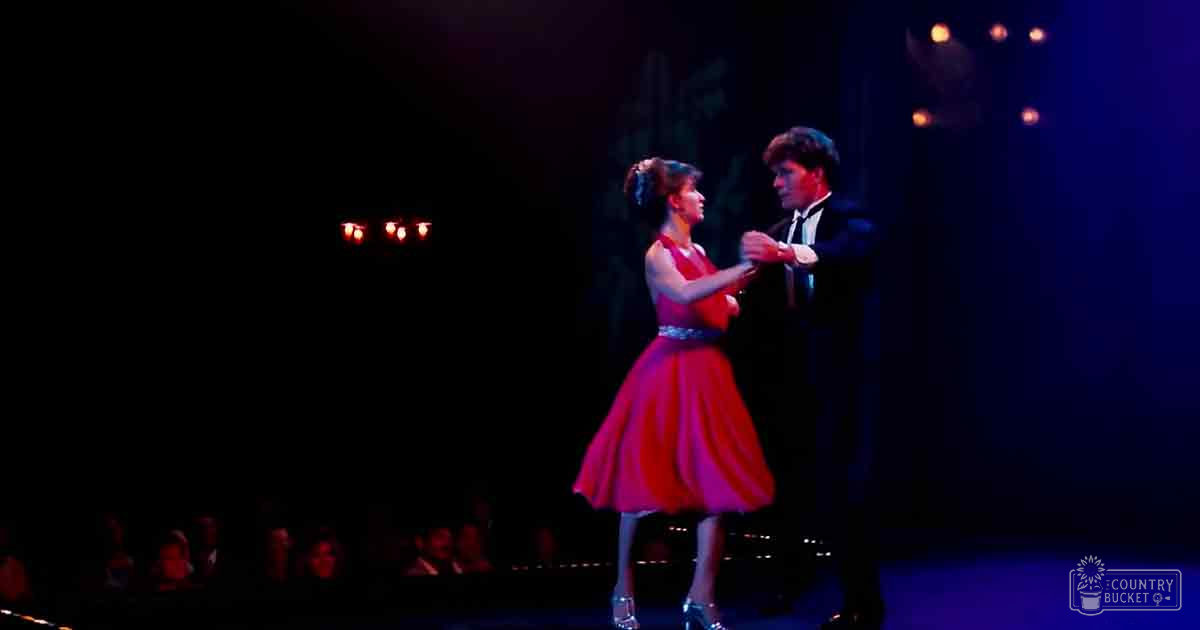 A dance scene on a dimly lit stage with blurred audience figures in the background, suggesting a mid-20th-century performance setting.