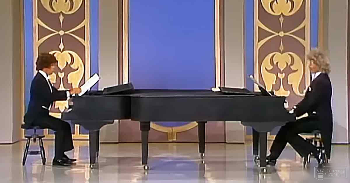 A duet performance scene with two grand pianos, ornate decorative panels, and a blue backdrop indoors on what appears to be a stage or set designed for an elegant room.