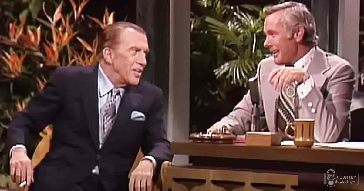 Two adults in a mid-20th century talk show studio, one wearing a dark suit with a patterned tie, the other in a light-colored suit jacket over a collared shirt.