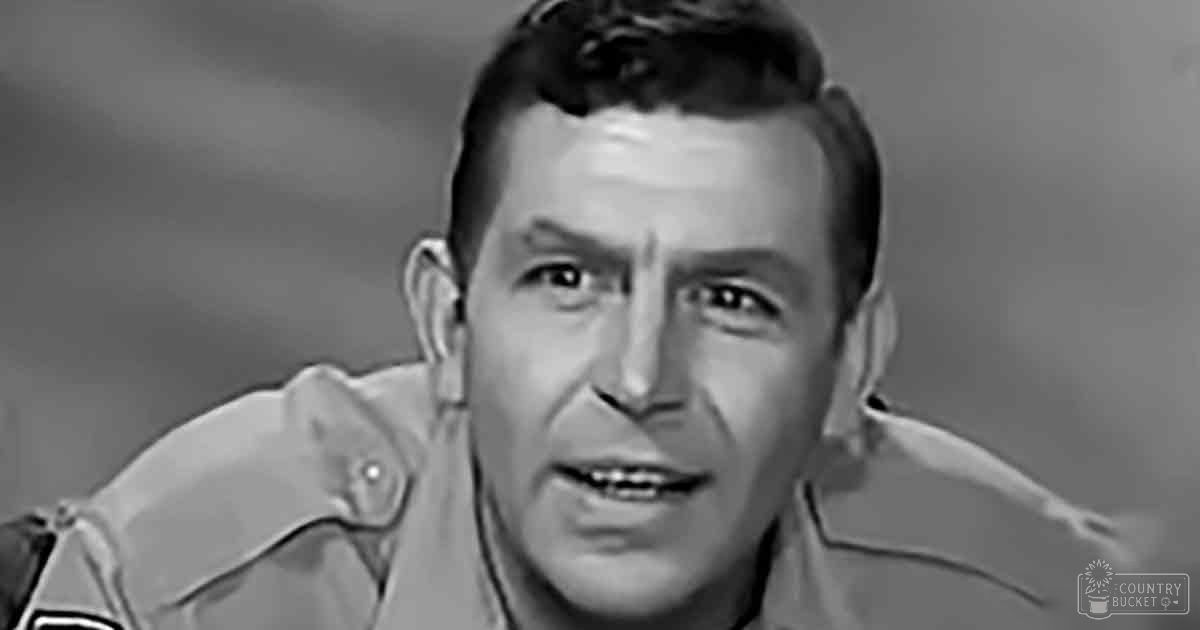 A middle-aged adult male wearing a light-colored button-down collared shirt in an indoor setting.