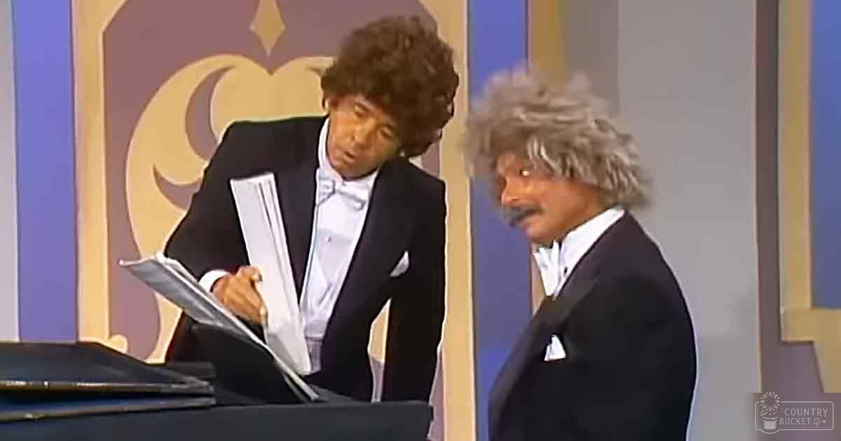 A comedic duo dressed formally in a studio with ornate background suggesting a late 20th-century stage setup.
