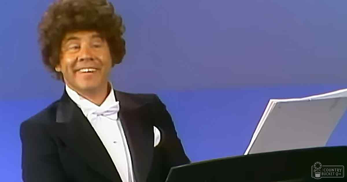 An adult male singer in a formal black tuxedo with white shirt and bow tie on stage with sheet music.