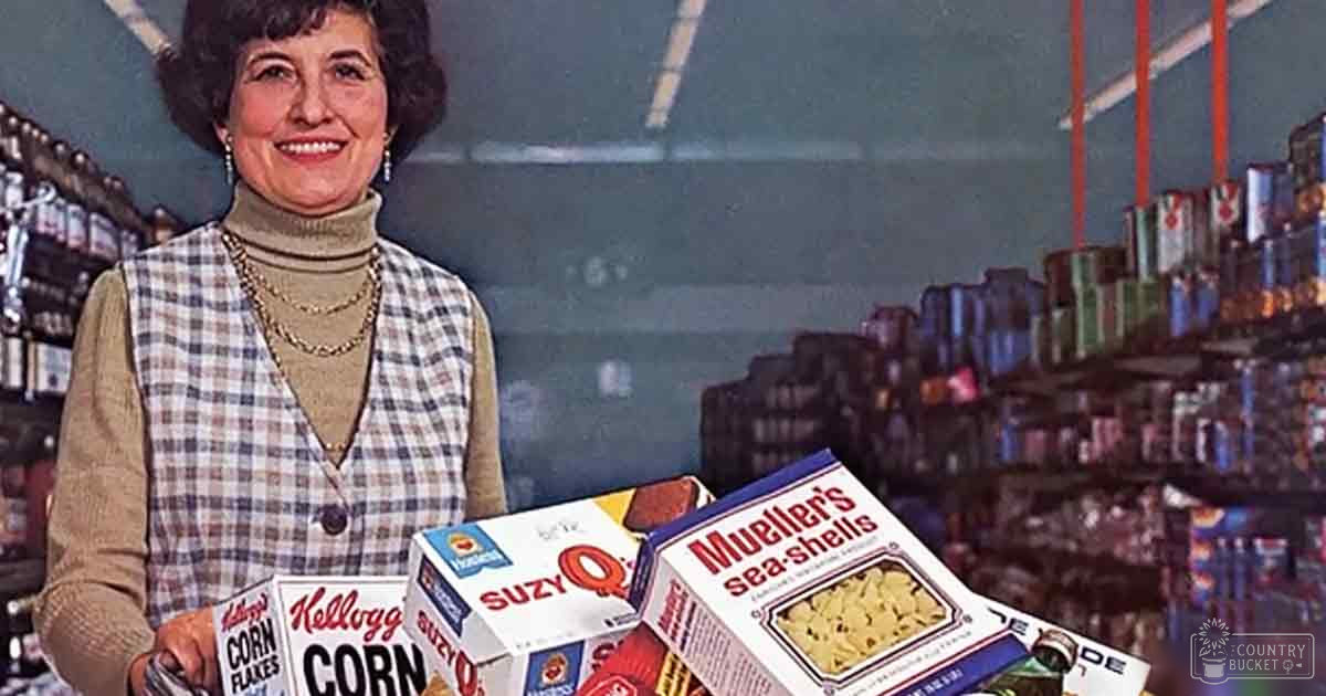A middle-aged to older adult woman wearing a plaid vest over a turtleneck sweater in an indoor grocery store setting, surrounded by various cereal and soda products.