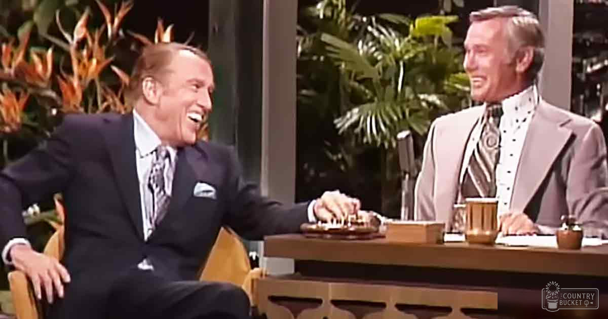 Talk show host and guest on a studio set with greenery and controlled lighting; spring or summer season suggested by plants.