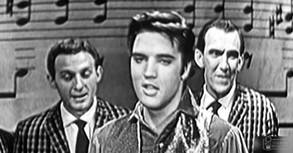 Elvis Presley stands center stage with two supporting men behind him; musical notation on the backdrop suggests a performance setting in an indoor environment.