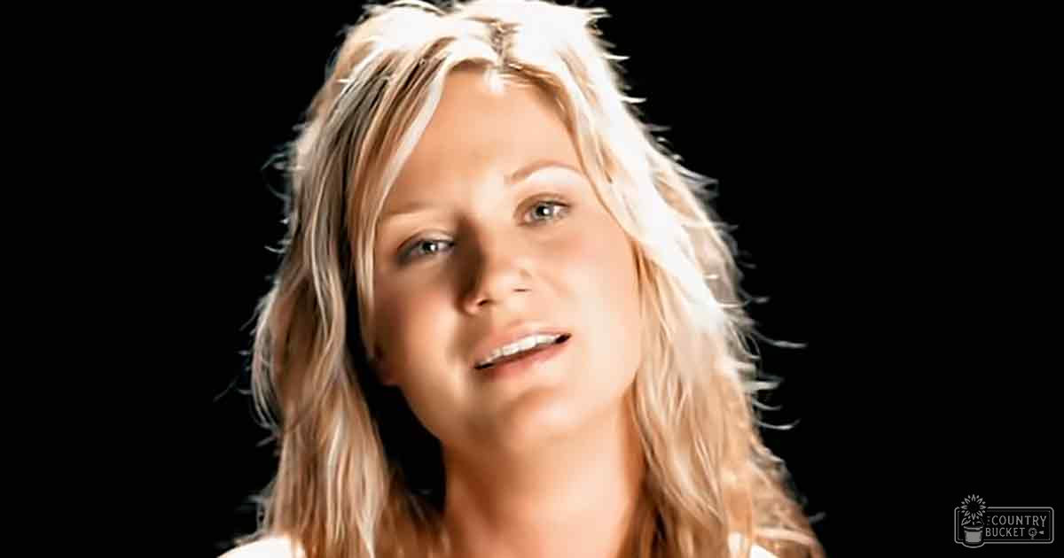 A young adult female wearing a white tank top against a dark indoor backdrop under studio lighting.