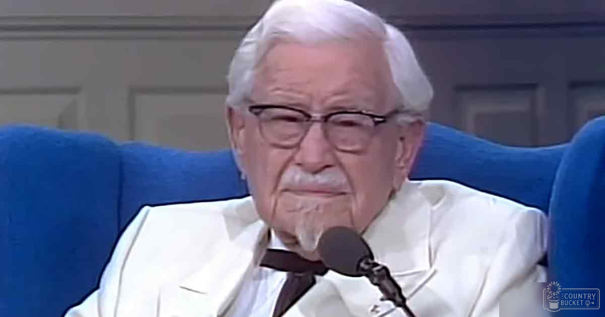 Older adult male in white suit with black bow tie, seated on blue armchair in indoor studio setting