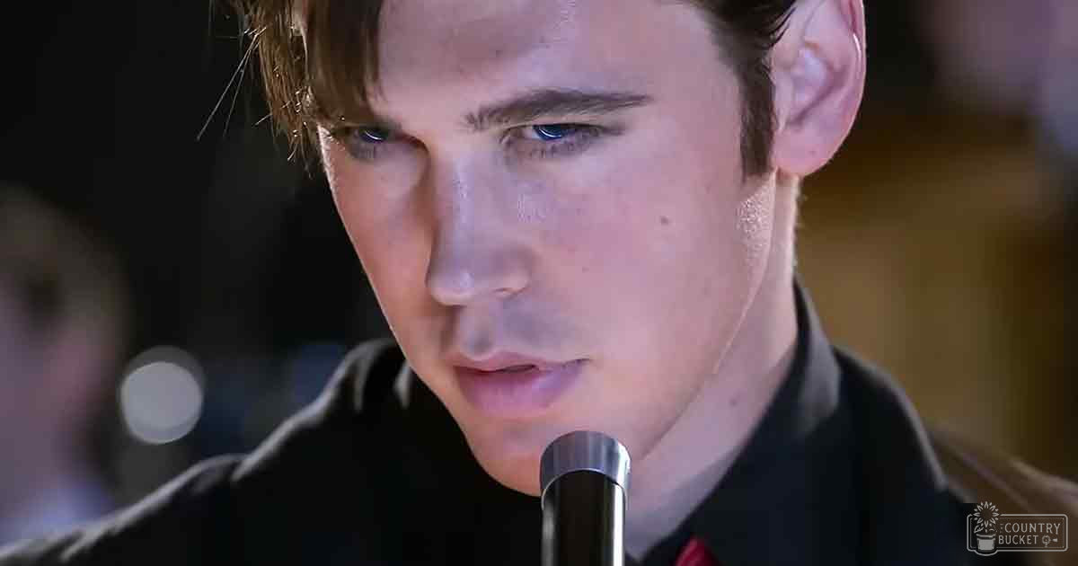 A young adult male wearing a fitted, dark-colored collared shirt indoors under artificial lighting.