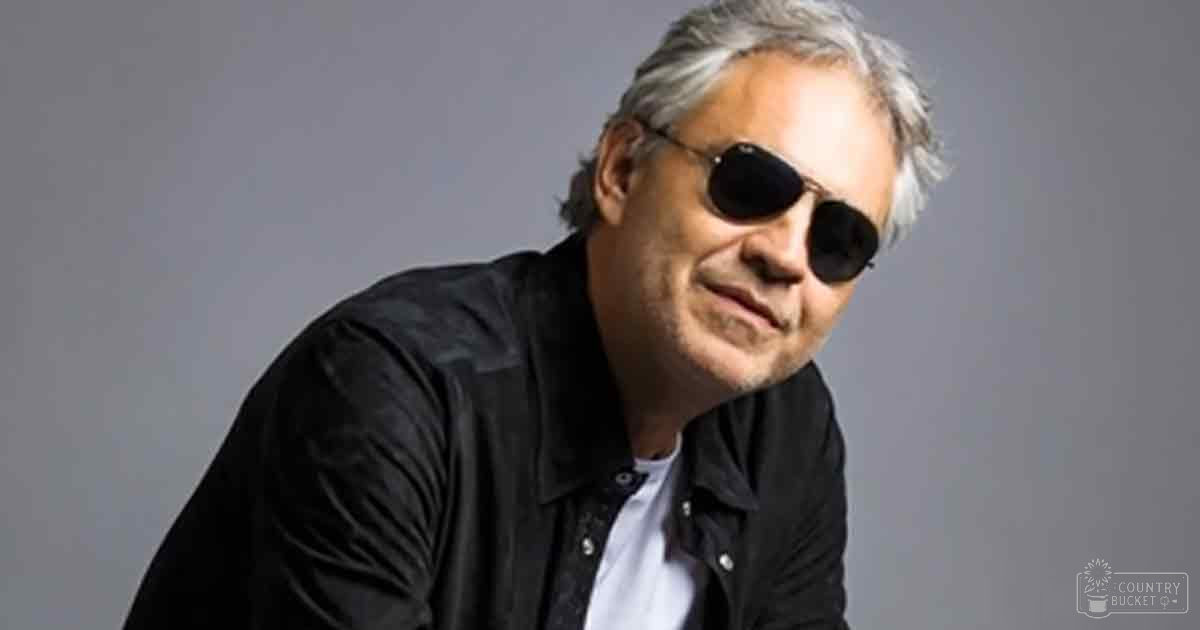 A middle-aged adult male wearing a relaxed fit, collared, long-sleeved black button-up shirt with dark sunglasses against a plain gray indoor background.