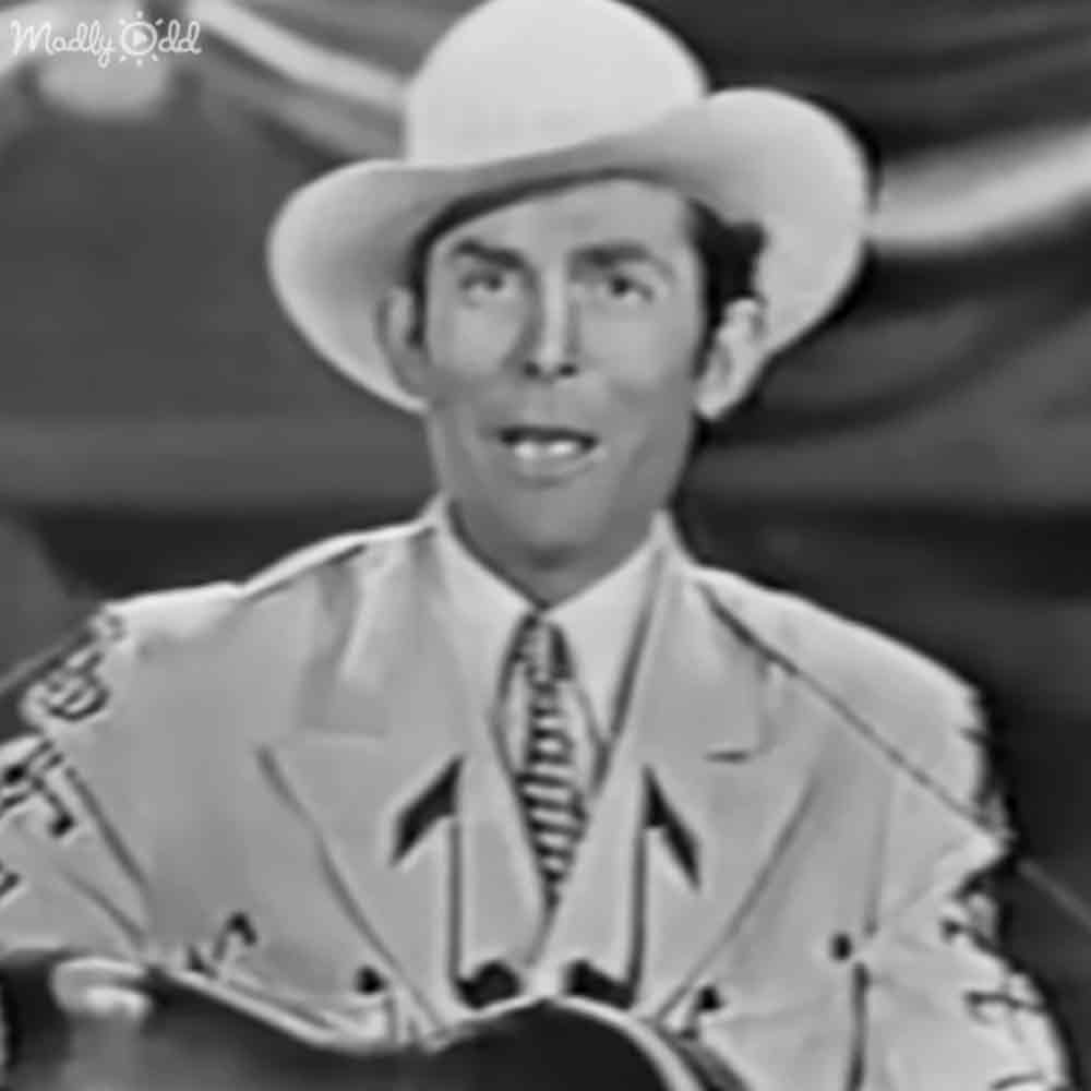 An adult male singer dressed in a mid-20th-century cowboy outfit indoors with a guitar partially visible.