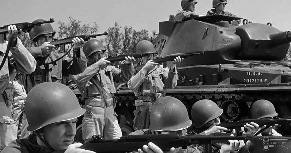 A group of young adult males in light-colored military uniforms with helmets are training outdoors under bright daylight, near a tank labeled "U.S.A."