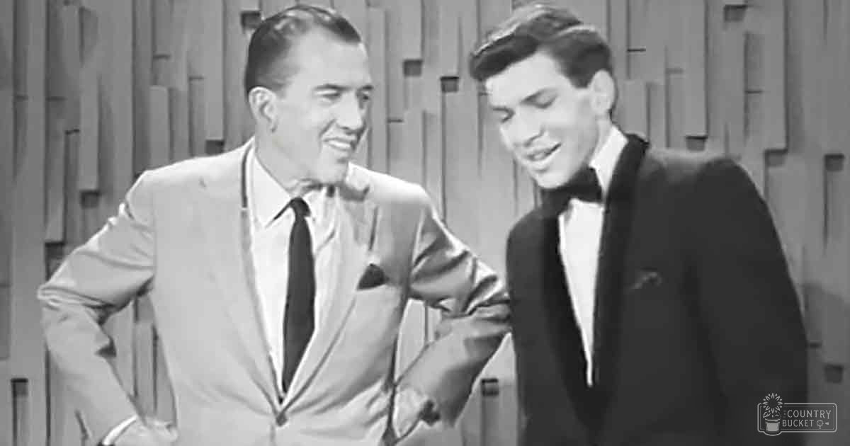 Two men in formal suits pose against a patterned backdrop, suggesting a mid-20th century television or radio broadcast studio setting.