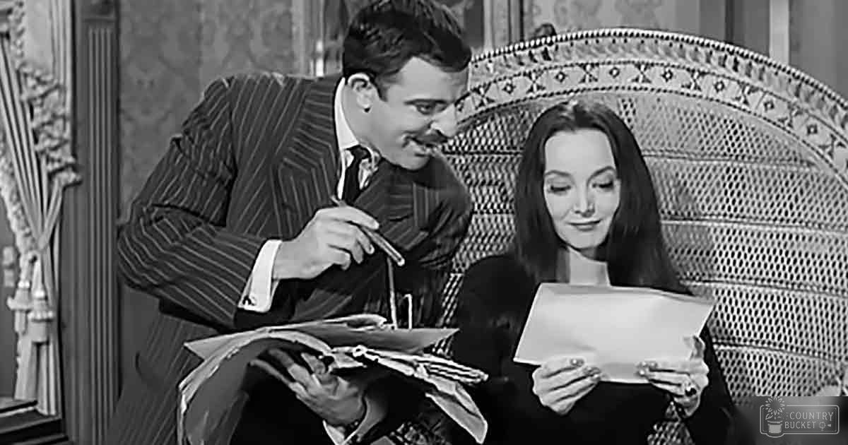 A scene from 'The Addams Family' in a mid-20th-century living room with ornate wallpaper and curtains, with two formally dressed characters.
