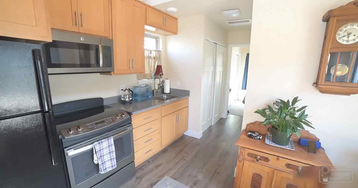 A residential kitchen scene with black appliances, wooden cabinets, a granite countertop, natural light, and daytime setting.