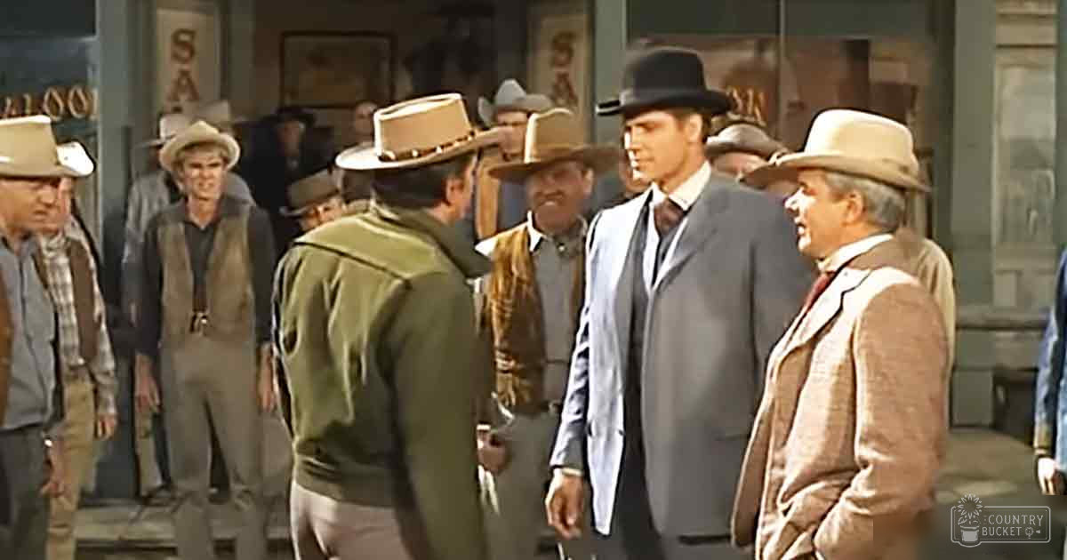 An outdoor scene in a Western town setting with adults dressed in period attire on a clear day.