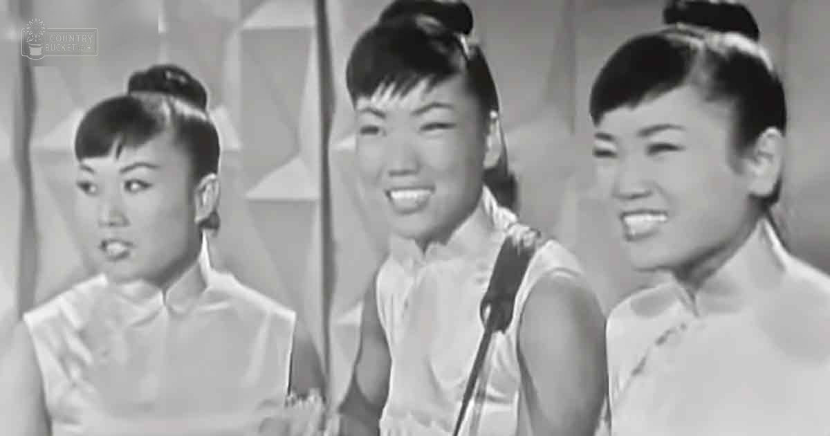 Group performance scene with mid-20th-century attire, likely from a film or TV show; indoor setting with curtains and microphone stand.