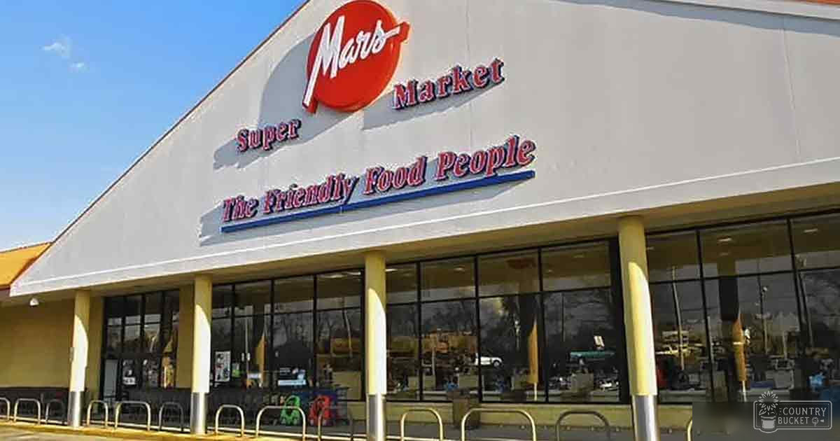 Exterior view of a Mars Super Market with large glass windows, metal bike racks, and visible signage reading 'Mars Super Market' and 'The Friendly Food People'.