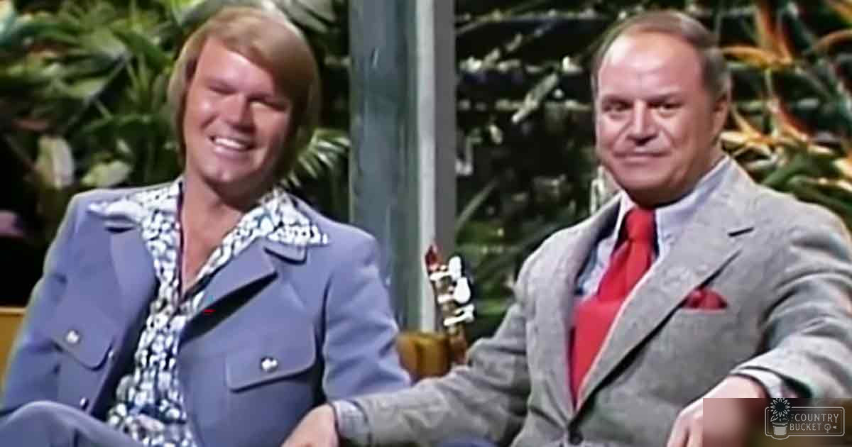 Two adult male figures dressed in mid-20th century attire stand against a backdrop of lush artificial greenery, suggesting an indoor studio setting designed to mimic nature.