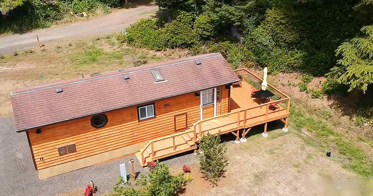Rural wooden cabin with deck, surrounded by greenery in daylight.