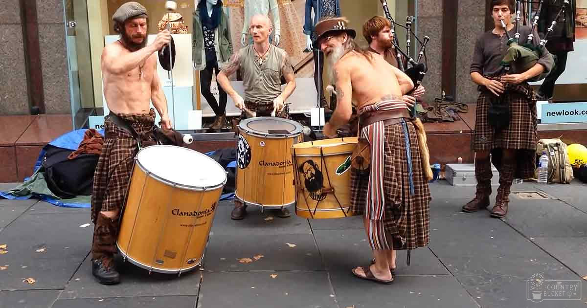 Street performance with musicians in traditional attire, urban setting, autumn leaves on ground.