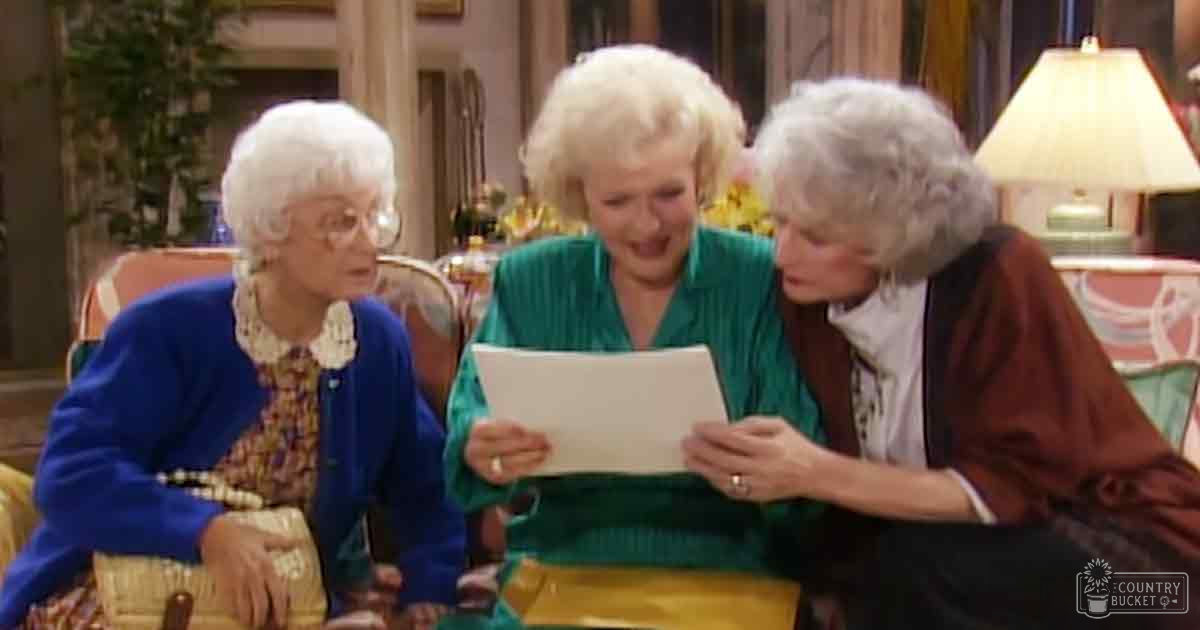 Three older adult females dressed casually in a cozy living room setting with natural light and visible home decor elements.