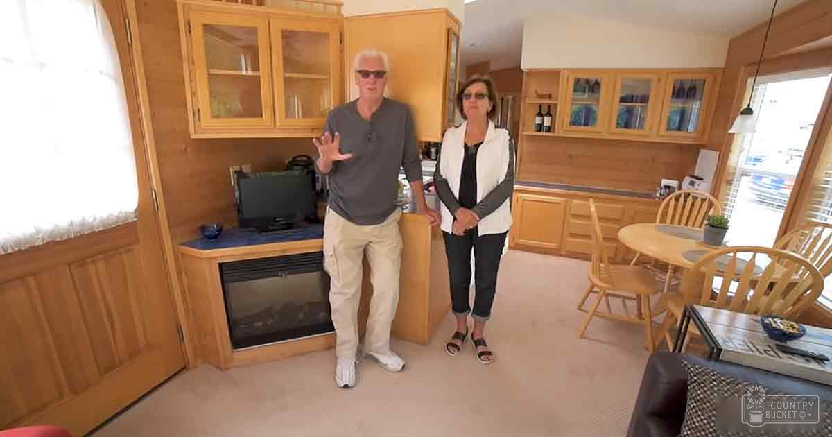 Middle-aged couple in casual attire indoors, surrounded by home furnishings and light natural lighting.