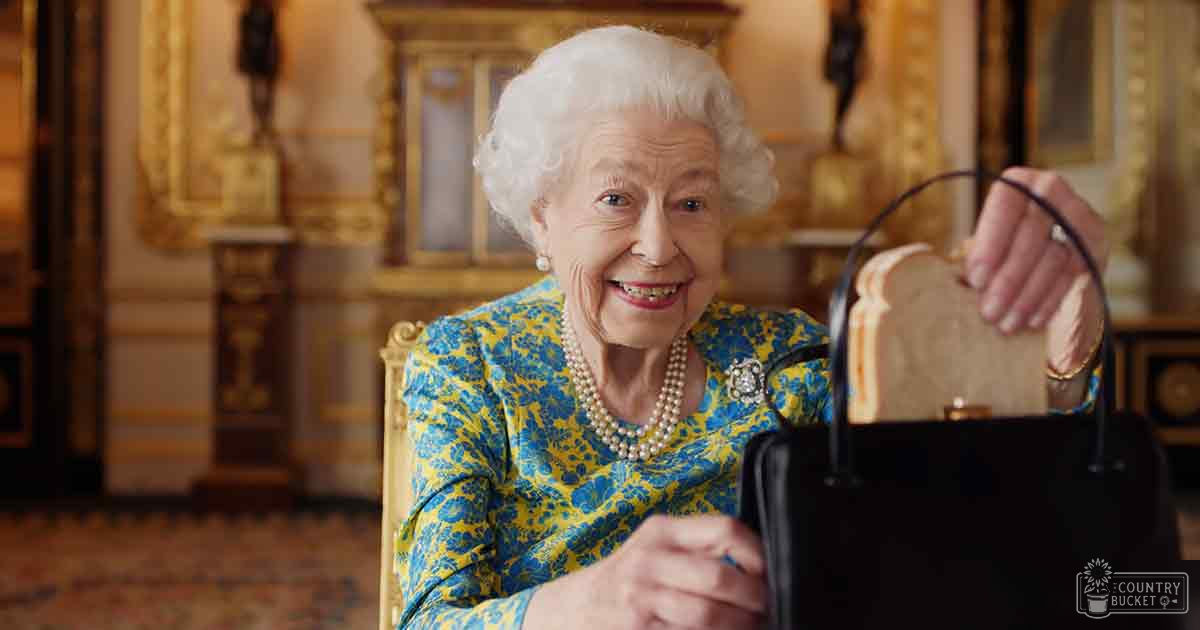 An older adult female wearing a blue and yellow floral dress with pearl jewelry, holding a black handbag, set against opulent grand palace decor.