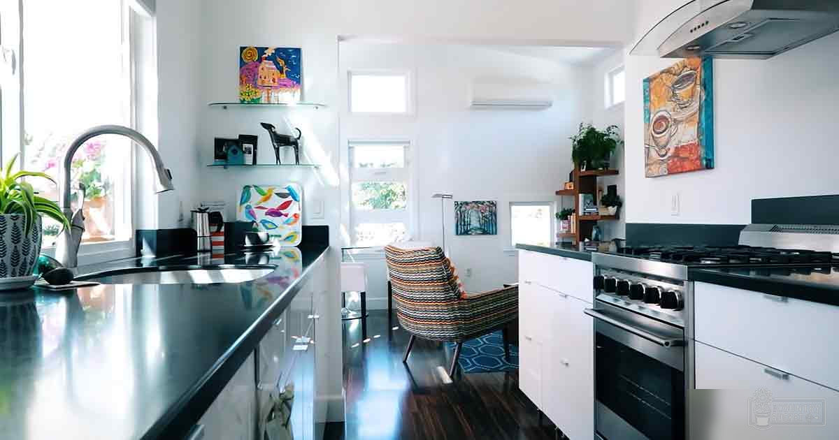 A modern kitchen with stainless steel sink, black countertops, white cabinets, decorative items like a bird-patterned cutting board and potted plant in a residential home setting