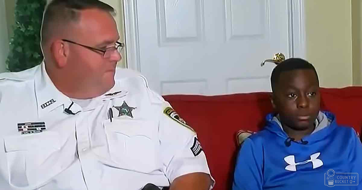 A law enforcement officer in a white uniform with patches, seated next to an 8-10-year-old child wearing a blue Under Armour hoodie indoors during the holiday season.