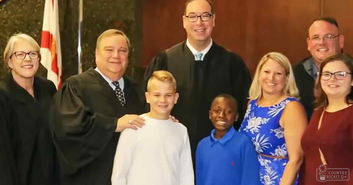 Group photo of adults and children in a courtroom setting with wooden paneling and a flag visible.